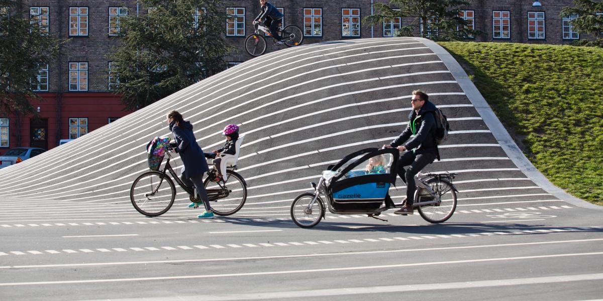 Kvinde med barnesæde på cyklen samt mand på ladcykle med barn i.